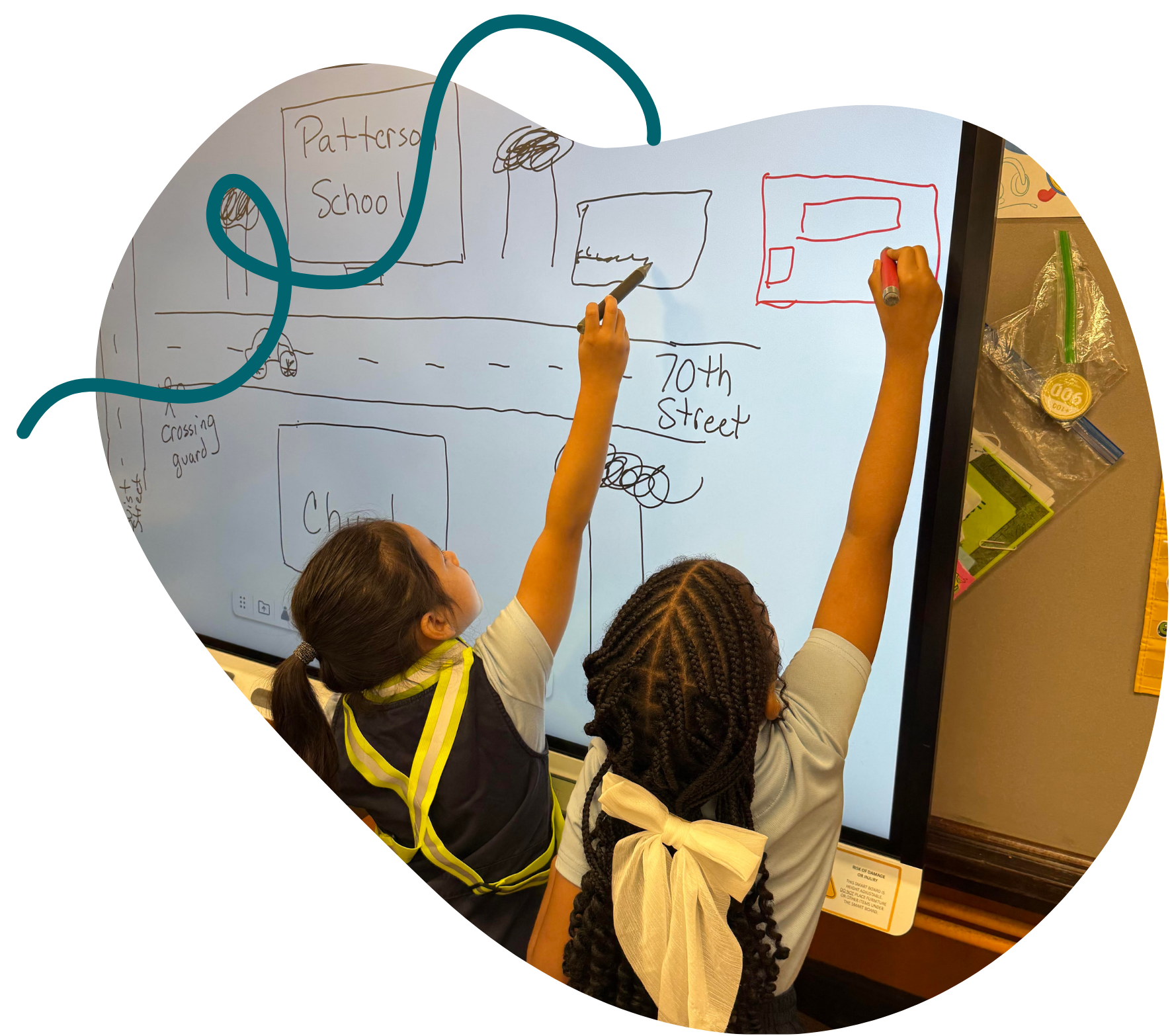 Two students collaborating on a hand-drawn town map at a whiteboard.